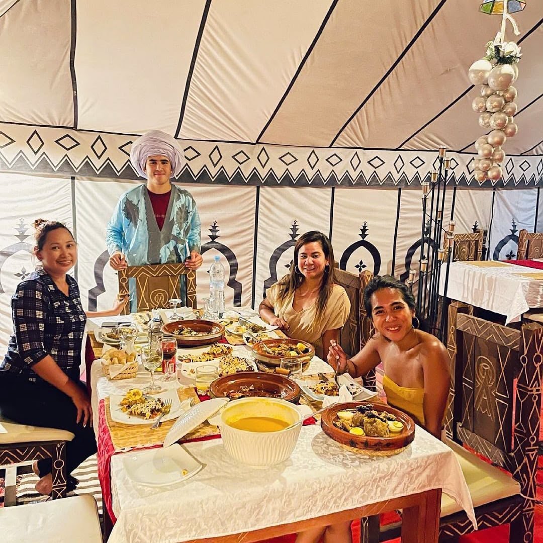 Guests enjoying a Moroccan dinner with tagines in the restaurant tent at Dihya Desert Camp, Merzouga